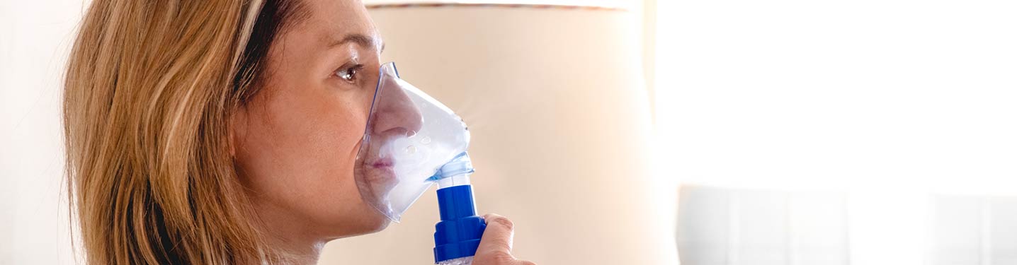 Woman laying in bed doing a nebulizer treatment.